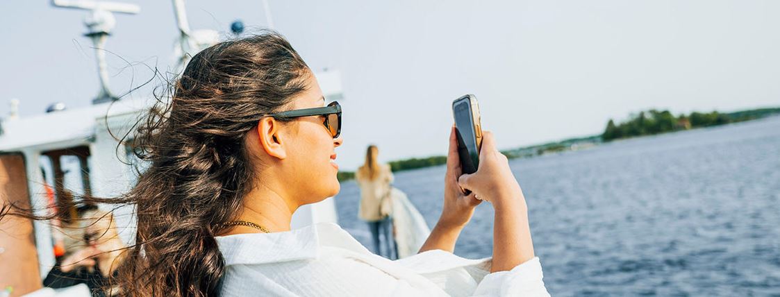 En kvinna står ombord på en båt och tar ett foto med sin mobiltelefon.