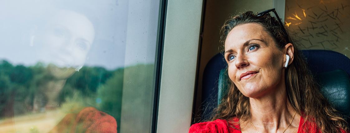 En kvinna sitter ombord på ett Öresundståg med hörlurar i öronen och blickar ut.