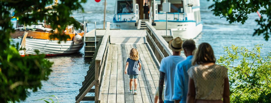 En pojke går längs en lång brygga mot en skärgårdsbåt.