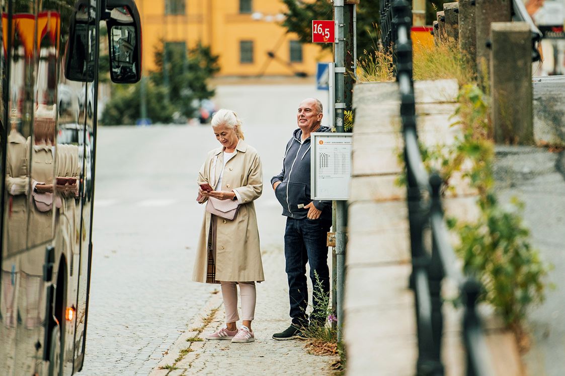 Resenärer väntar på bussen vid hållplats.