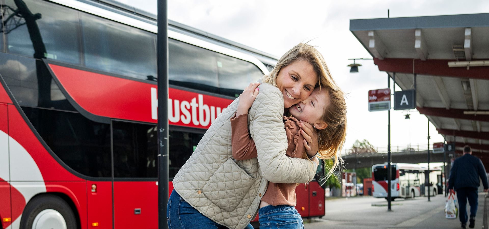 Kvinna och barn kramar varandra framför kustbuss på Ronneby station.