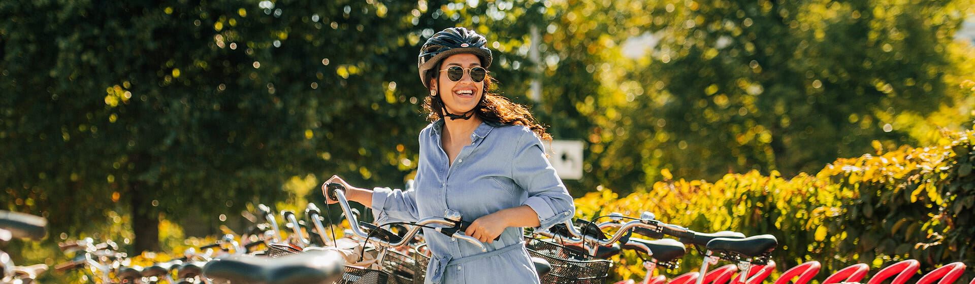 En kvinna med solglasögon och cykelhjälm håller i en cykel.