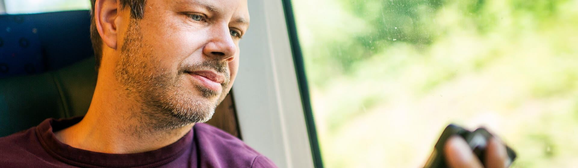 En man med skäggstubb sitter ombord på ett Öresundståg och tittar i mobiltelefonen.