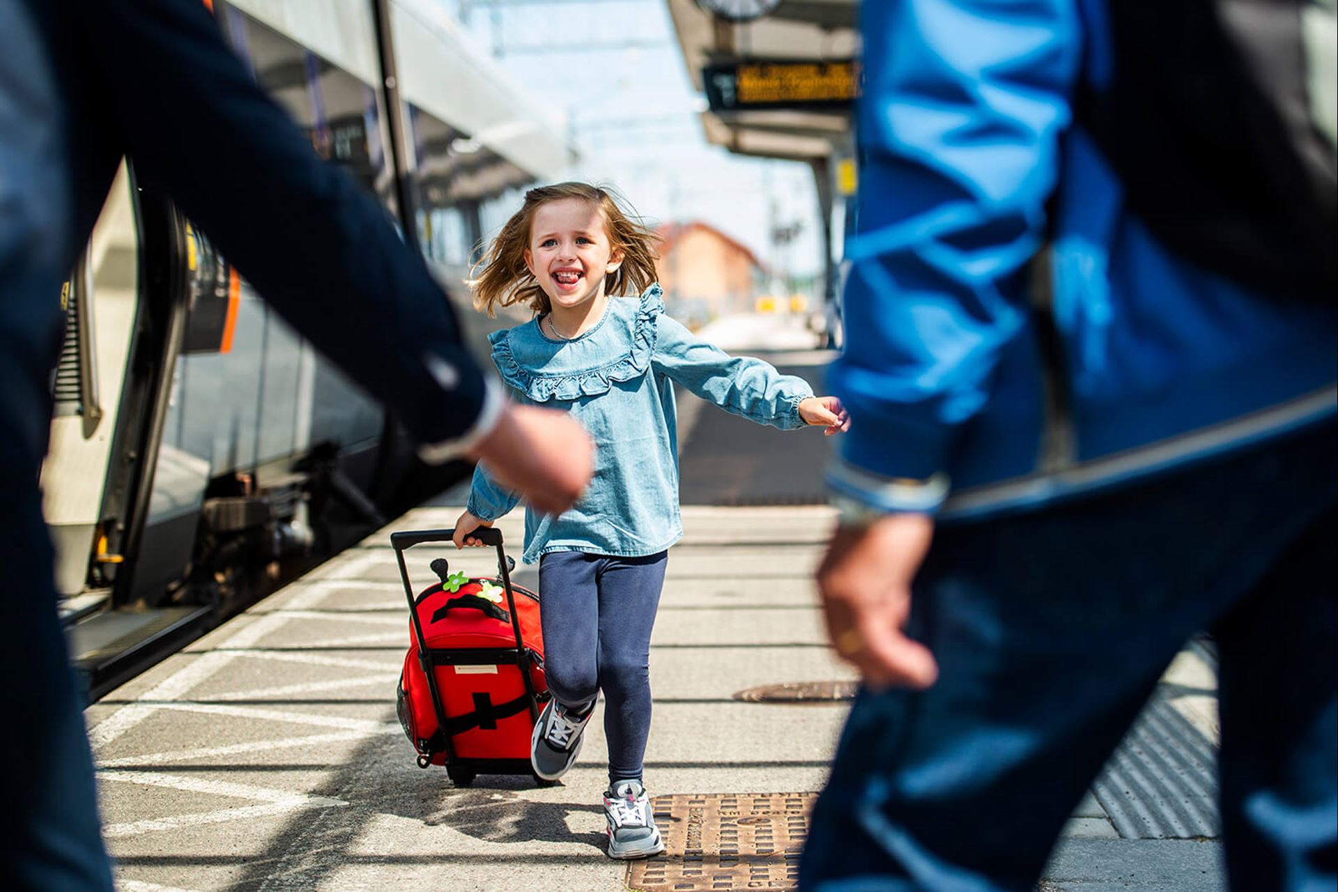 En flicka springer från tåget mot två personer med öppna armar.